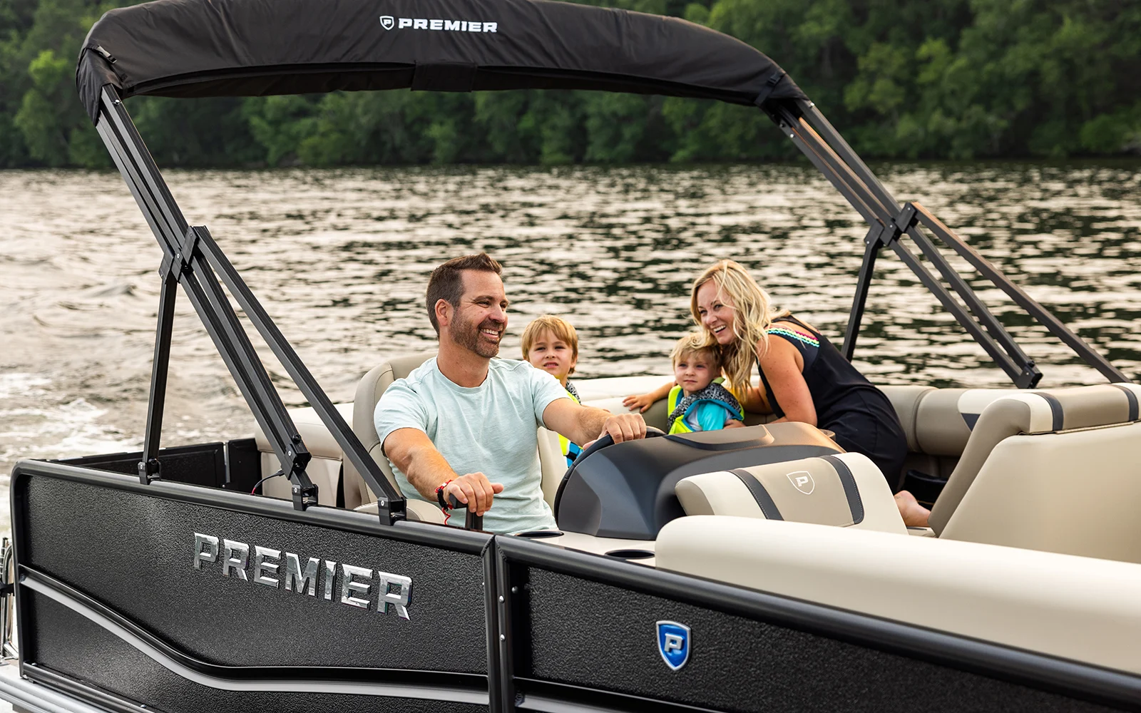 Family enjoying a day on a Premier pontoon boat with plush seating, Bimini top, and spacious deck cruising on a calm lake