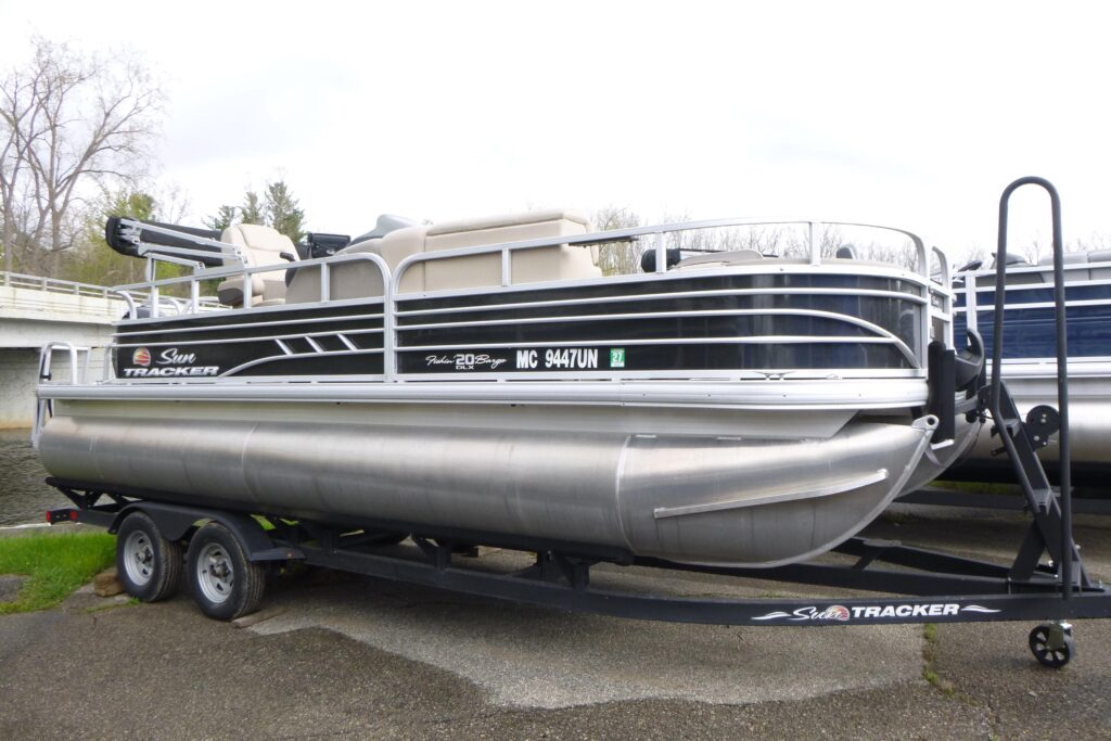 2021 Sun Tracker Fishin’ Barge 20 DLX pontoon boat on trailer with fishing seats and aluminum pontoons.